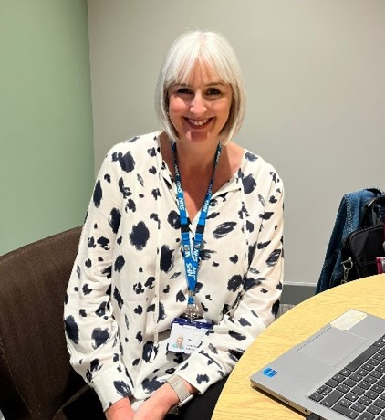 Lady with a blonde bob wearing a black and white blouse sitting smiling to the camera