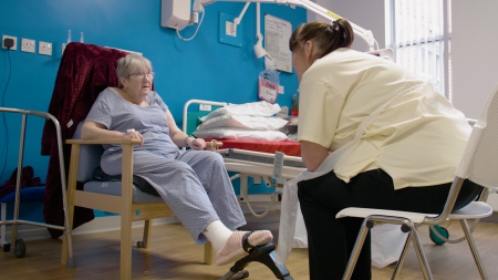 A patient sat in a chair using a foot pedal, with a member of staff watching on.