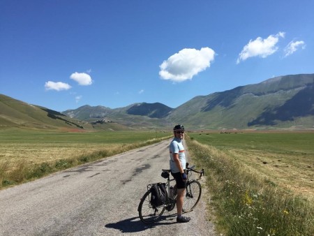 A man standing with his bike in front of some hills and blue sky.