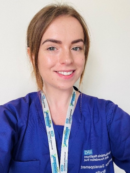 Selfie of a girl wearing purple scrubs smiling to the camera