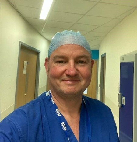 A portrait of a man wearing blue scrubs and a scrub cap