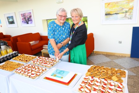 Two ladies stand behind a buffet table and cut a celebration cake 